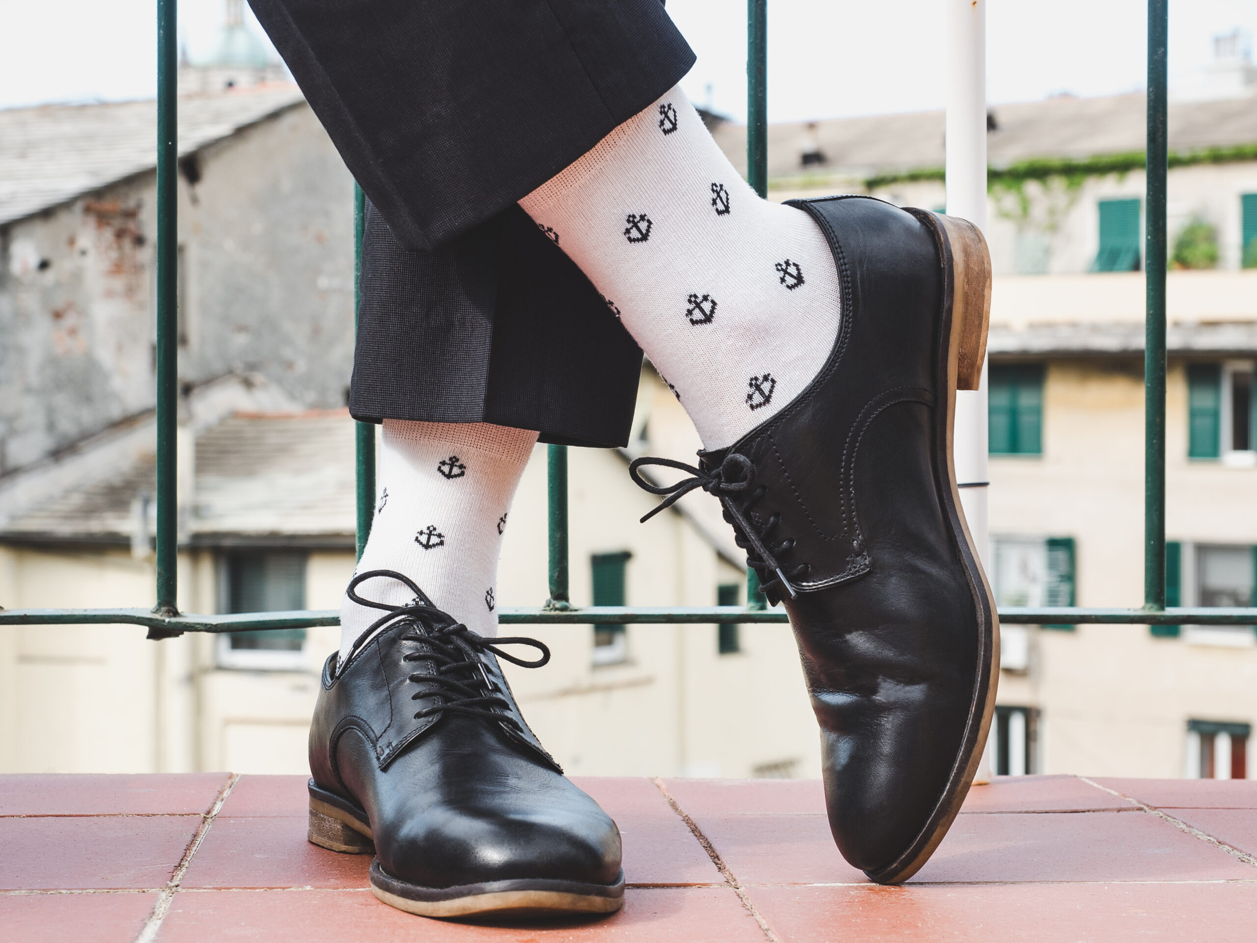 Men's legs, stylish shoes, colorful socks with a pattern in the form of anchors on the background of the street and houses. Concept of style, fashion and beauty